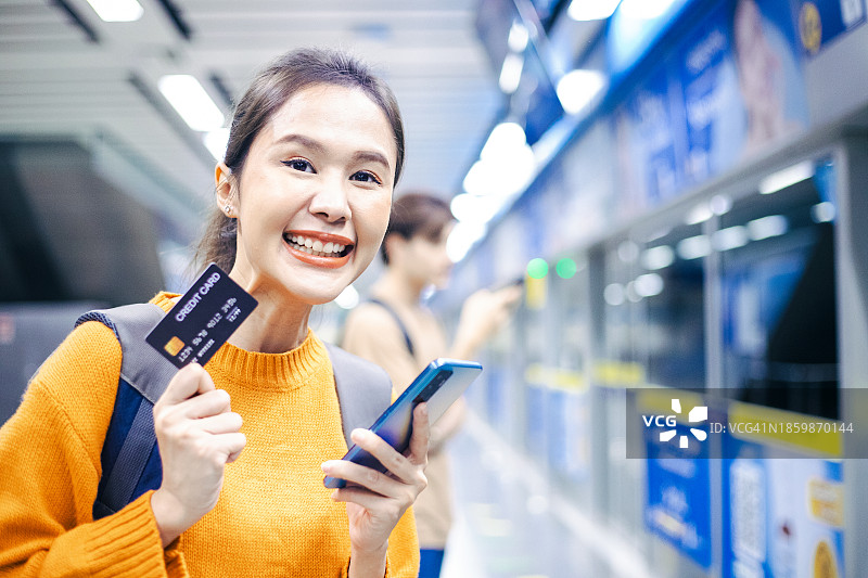 年轻女子用信用卡支付车票，并在候车时查看电子邮件图片素材