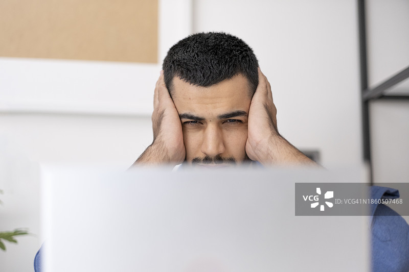 年轻男人牙痛的特写。英俊的年轻男人在家里的办公室用电脑时，摸着脸颊，因牙痛而感到痛苦。图片素材