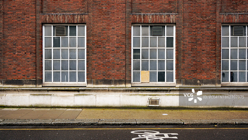 英国伦敦带有不透明窗户、人行道和自行车道的风化砖墙图片素材
