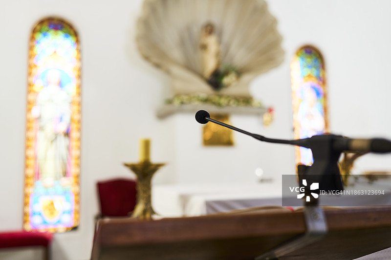 放置在阅读桌上的麦克风，背景是教堂内带有彩色玻璃设计的高大窗户，但已模糊图片素材