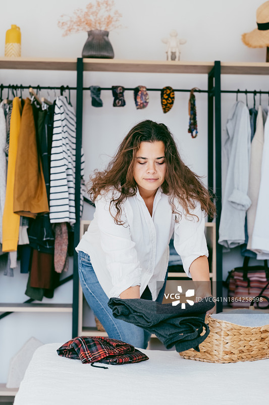 年轻女子在整洁的卧室衣柜里叠衣服，展示家居收纳图片素材
