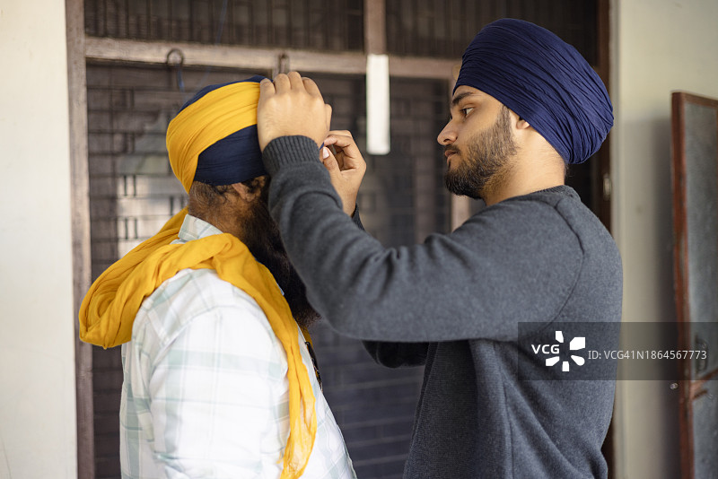在Lohri节之际，年轻锡克教男子帮助父亲系头巾图片素材