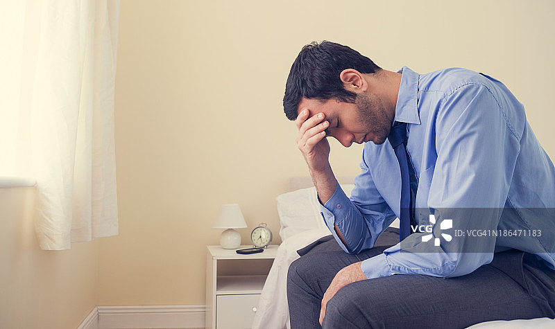 沮丧的男人抱头坐在床上图片素材