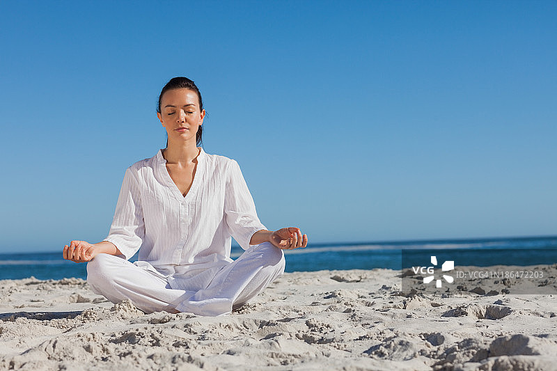 身穿白色衣服的女人在海滩上做瑜伽图片素材