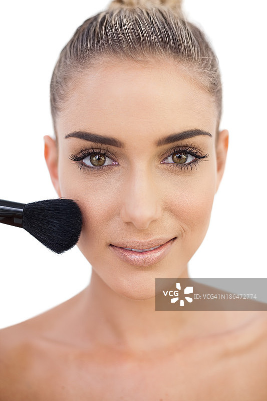 微笑的女人在脸颊上扑粉图片素材