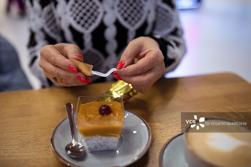 一位女士拿着金色包装的中国幸运饼干坐在咖啡馆的甜点桌旁图片素材