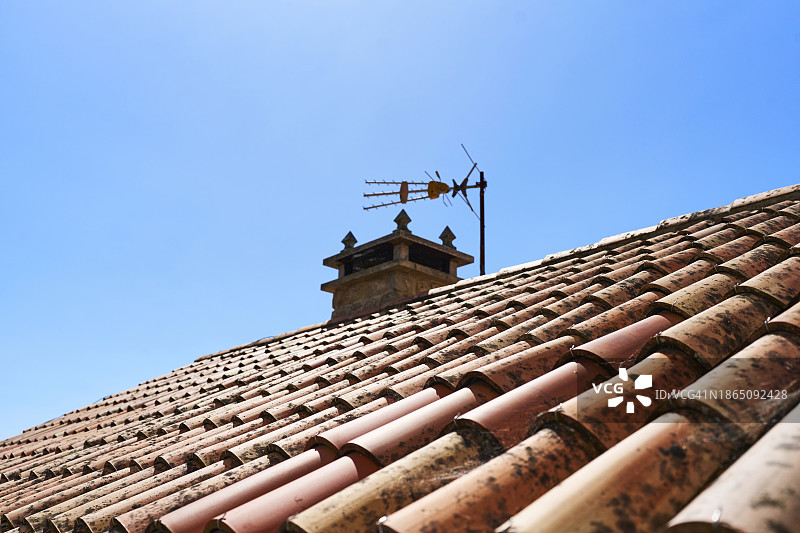 覆盖着红色瓷砖的屋顶，顶部有一个烟囱，背景中有一个天线，可以俯瞰蓝天。图片素材