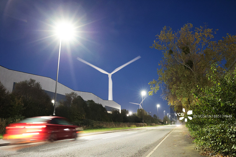 黄昏时分，汽车在有风力涡轮机的道路上飞驰图片素材