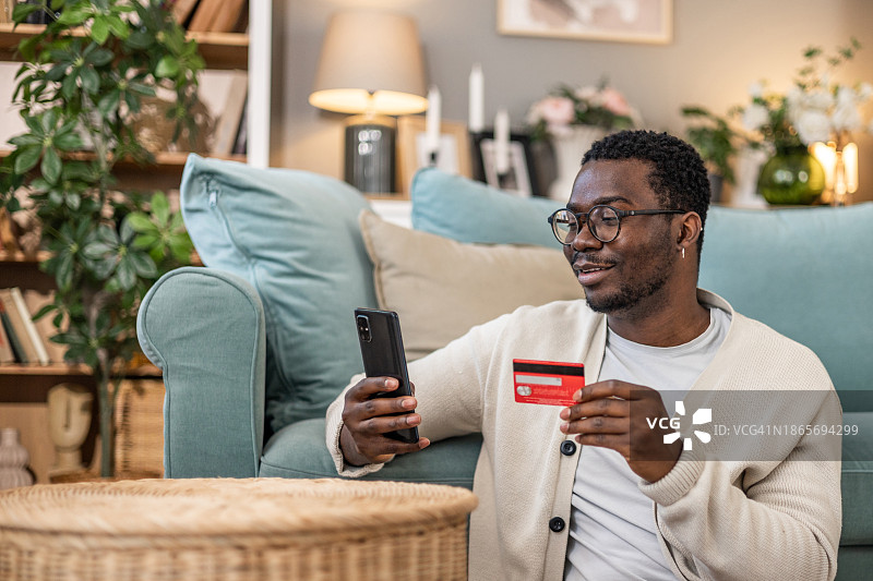 快乐的年轻男子使用信用卡和手机进行在线支付的肖像图片素材