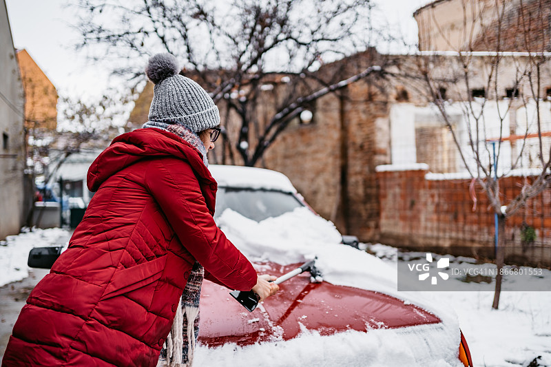 年轻女人清理汽车上的积雪图片素材