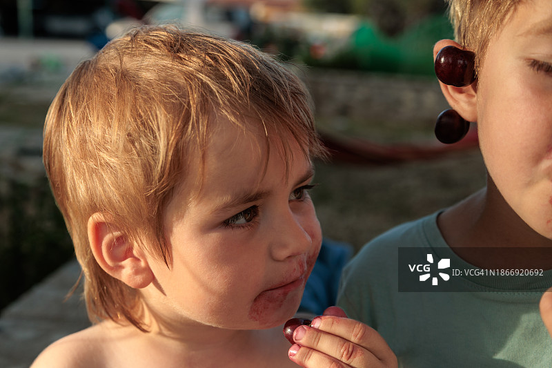 可爱的好奇幼儿男孩品尝成熟的樱桃，看着他哥哥吃东西。图片素材