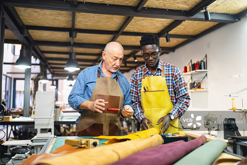 在皮革作坊里向老裁缝学习手艺的黑人青年图片素材