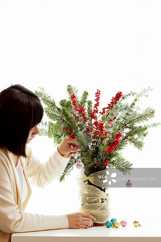 制作圣诞花束装饰的女人特写：冷杉枝、冬青果、桉树和圣诞小饰品图片素材