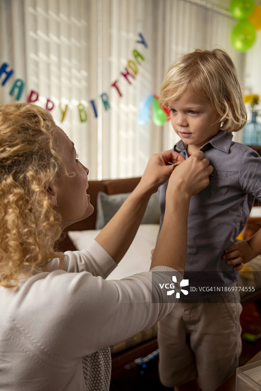 母亲帮助儿子穿衣服参加生日庆祝活动图片素材