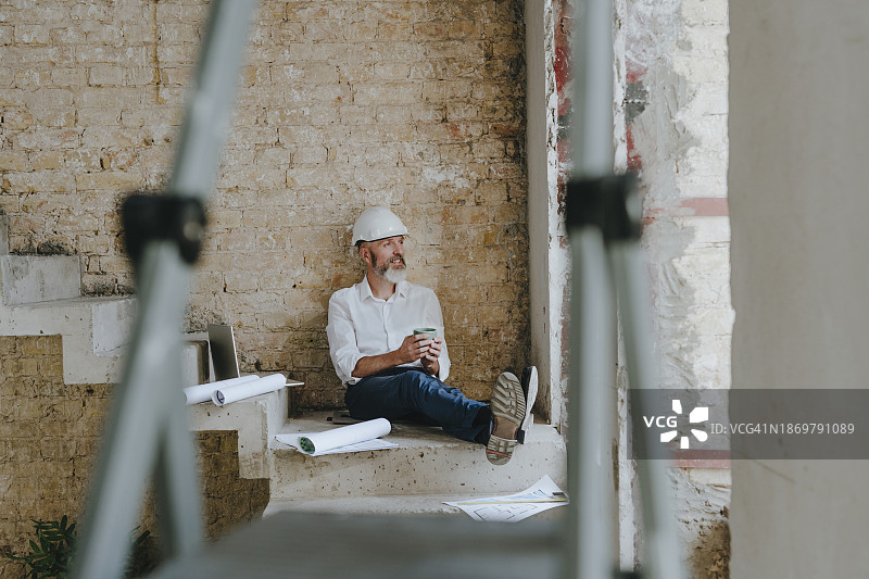 手持咖啡杯坐在台阶上看蓝图的沉思建筑师图片素材
