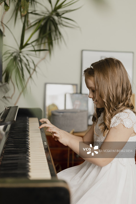 穿着白色连衣裙的女孩在家弹钢琴图片素材