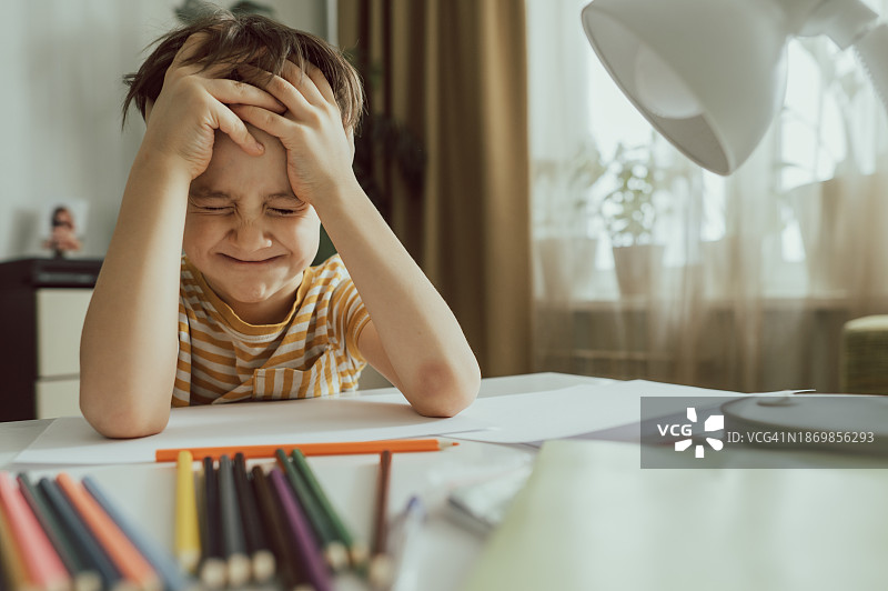 闭着眼睛坐在桌旁的忧郁男孩图片素材