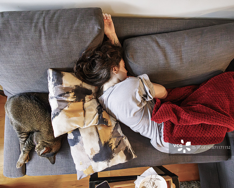 猫和女人午间小憩：猫和主人在不眠之夜后蜷缩在沙发上睡觉图片素材