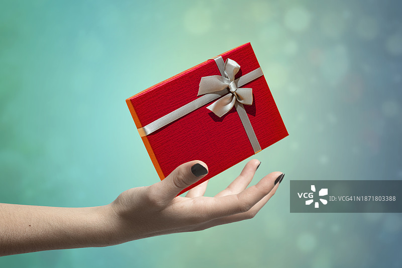 女人的手拿着系着银色丝带的红色圣诞礼盒图片素材