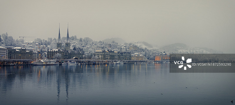 雾蒙蒙的冬日清晨，琉森湖畔覆盖着白雪的教堂和酒店图片素材