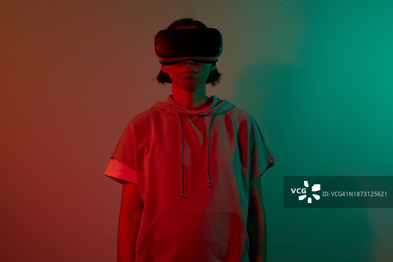 佩戴VR眼镜的年轻女孩在红绿色霓虹灯下的面部表情图片素材