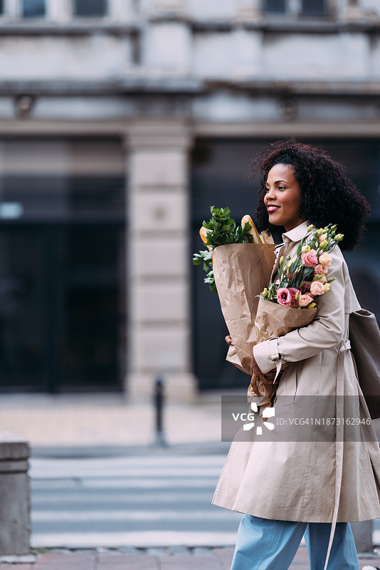 快乐的购物狂欢：容光焕发的女人带着食品和鲜花图片素材