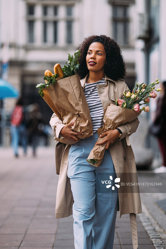 快乐的购物狂欢：容光焕发的女人带着食品和鲜花图片素材