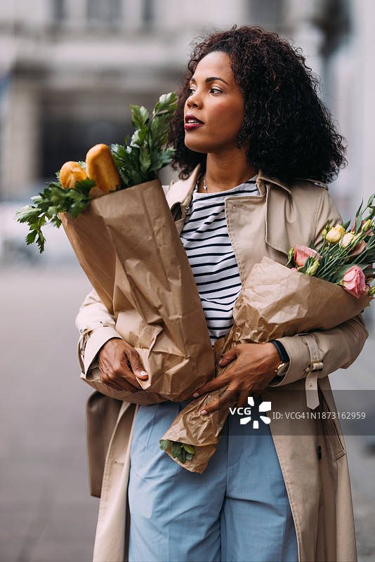 快乐的购物狂欢：容光焕发的女人带着食品和鲜花图片素材