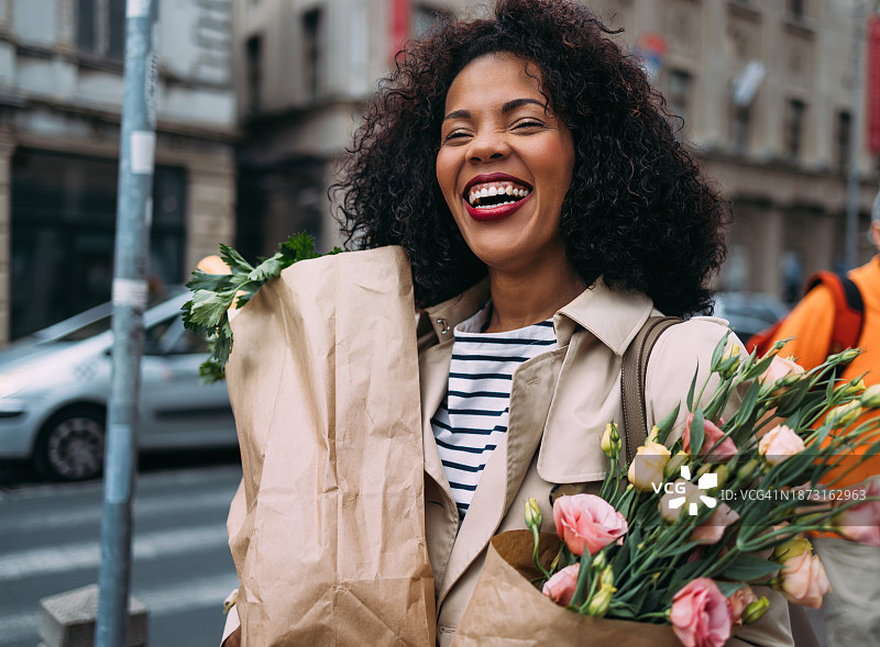 快乐的购物狂欢：容光焕发的女人带着食品和鲜花图片素材