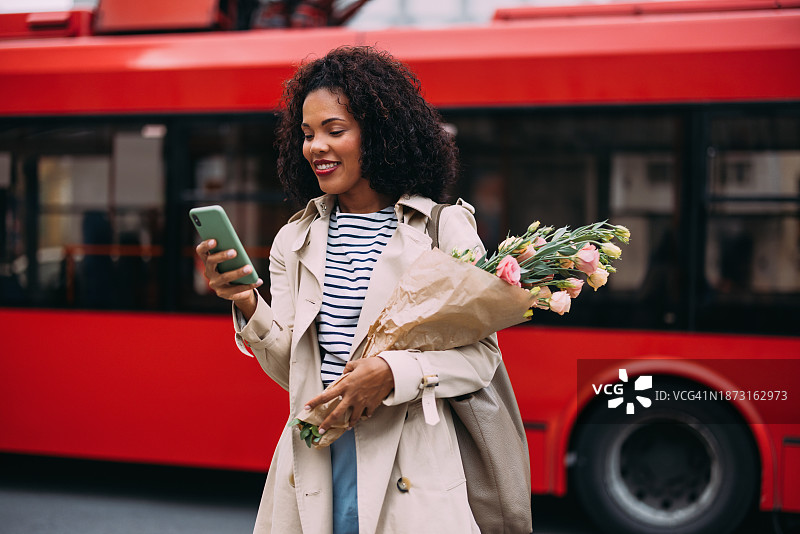 互联的跑腿：微笑的女人在街上玩弄杂货和电话图片素材