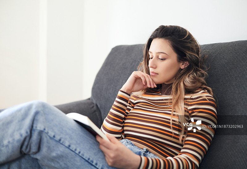 在家看书的漂亮女人，她正坐在沙发上放松图片素材
