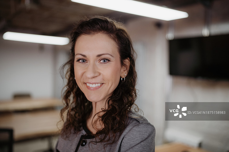 年轻女人自信地微笑，站在一个令人愉快的办公环境中图片素材