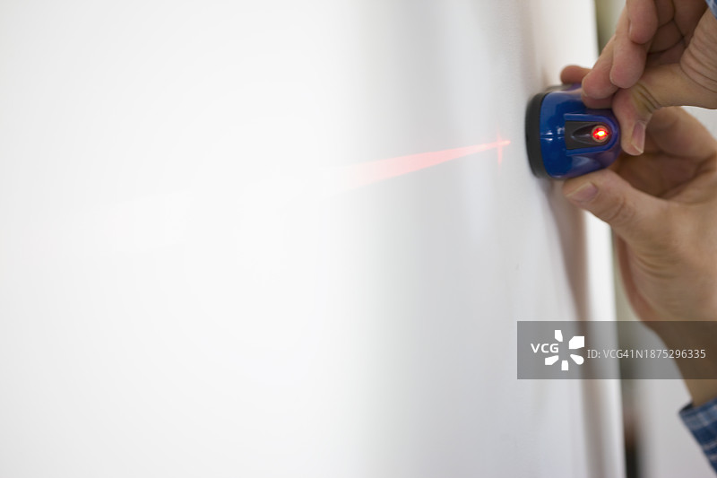 男人手持激光水平仪靠在白墙上图片素材