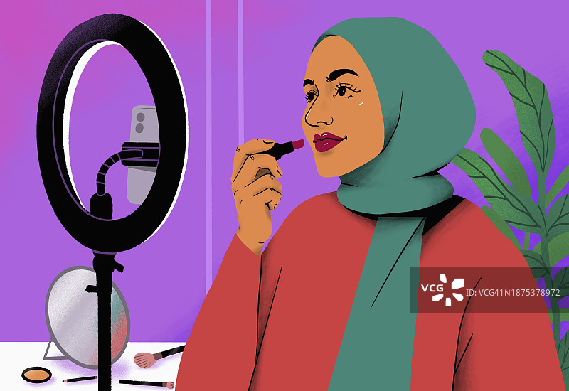 戴头巾的女网红在环形灯和智能手机后进行口红化妆教程图片素材