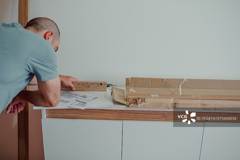 男人背对着镜头阅读组装家具的说明书图片素材