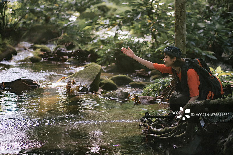 年轻的亚洲女子在河岸边深蹲，在热带雨林中泼水图片素材