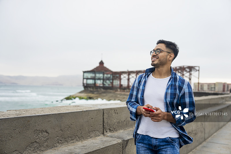 快乐的年轻拉丁美洲男子沿着秘鲁卡亚俄海滩的海岸线行走图片素材