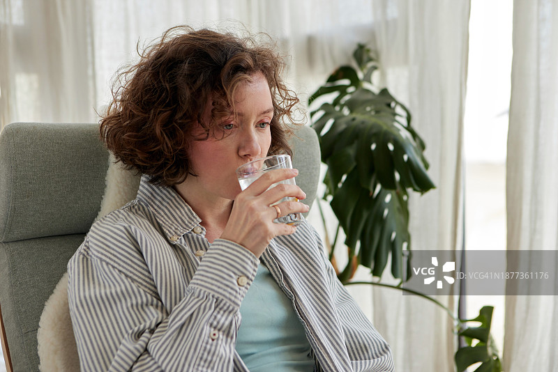 在家中坐在椅子上喝水的卷发女人图片素材