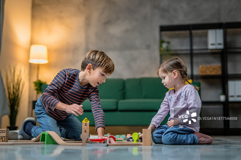 兄妹在家里的地板上玩木制火车玩具，儿童玩耍和学习概念图片素材