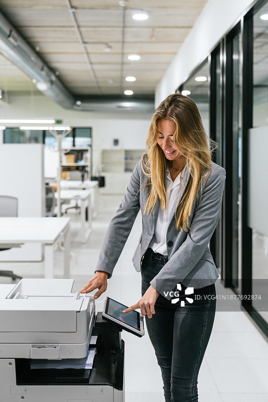 在现代工作空间中使用办公打印机和平板电脑的职业女性图片素材