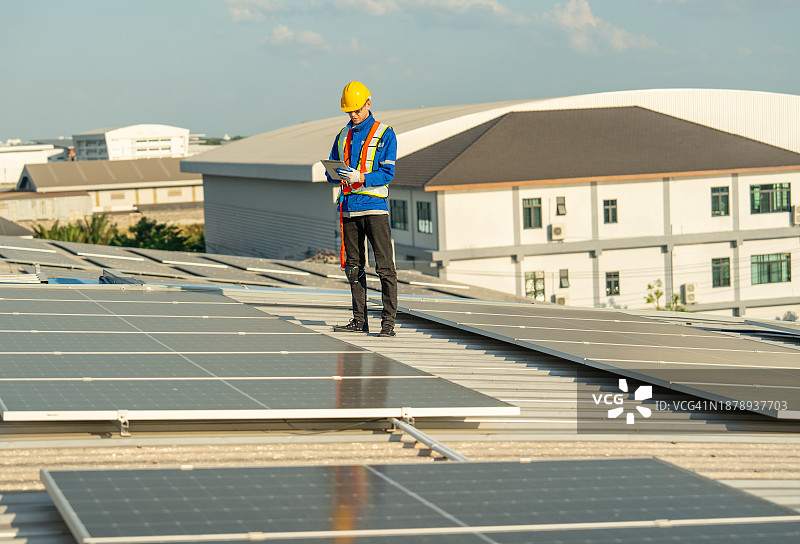 年轻技术员使用平板电脑在屋顶检查和维护太阳能电池板图片素材