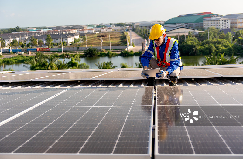 资深技术员手持平板电脑坐在屋顶，检查和维护建筑物或工厂的太阳能电池板图片素材