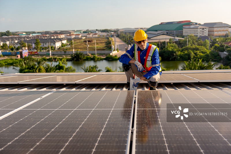 年长的技术员手持平板电脑坐在屋顶上，检查和维护建筑物或工厂的太阳能电池板图片素材