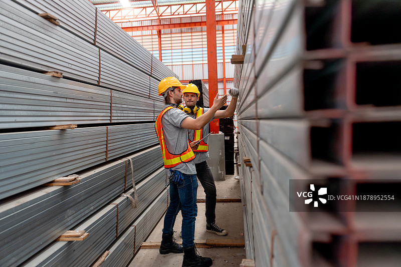 两位工厂工人在堆叠的钢管之间讨论工作图片素材