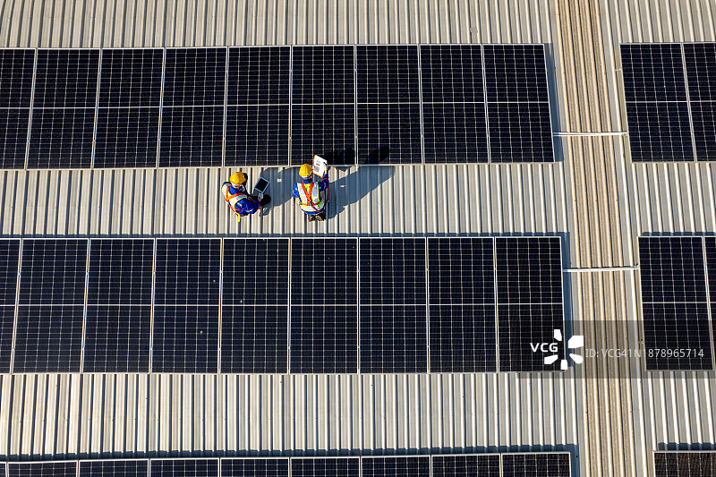 无人机视角：工人在工厂屋顶检查和维护太阳能电池板，绿色能源理念图片素材