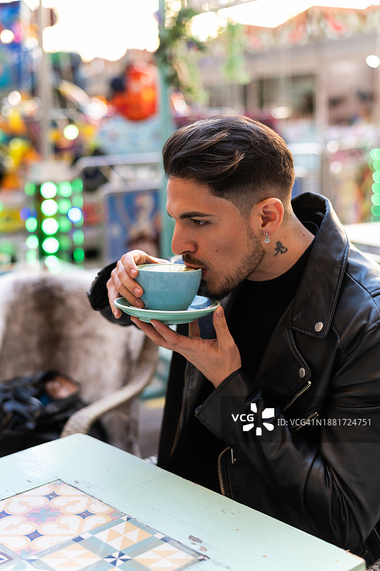 年轻男人坐在户外咖啡馆里喝咖啡图片素材