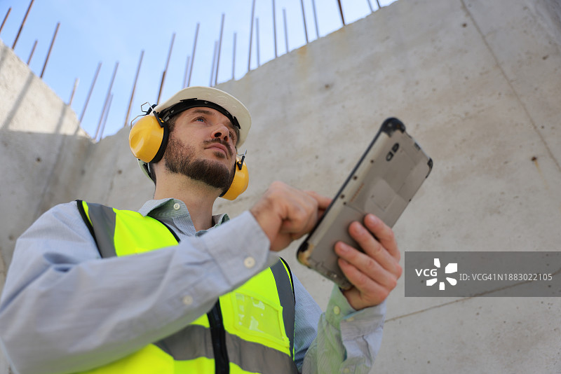 土木工程师身穿绿色反光安全夹克和耳罩，在工地上巨大的管道中工作图片素材