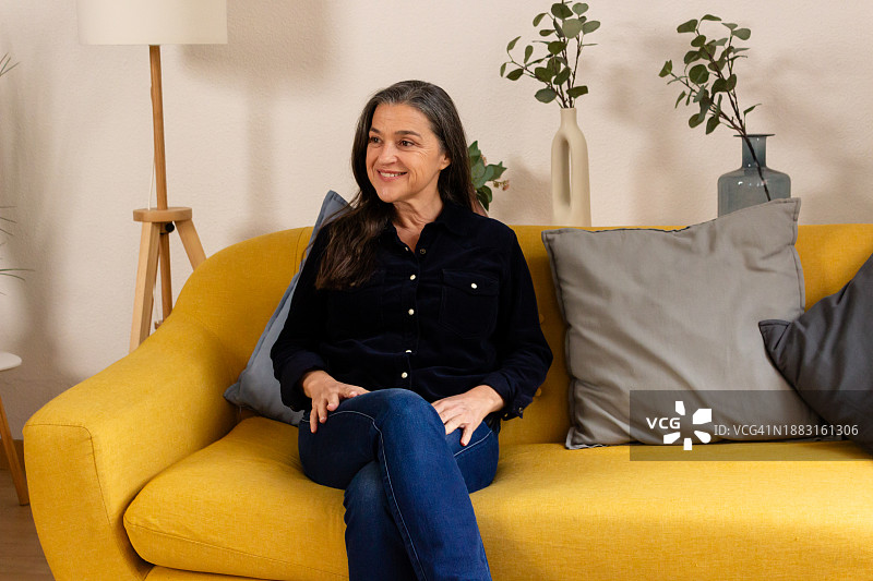 在家坐在黄色沙发上的中年妇女肖像图片素材