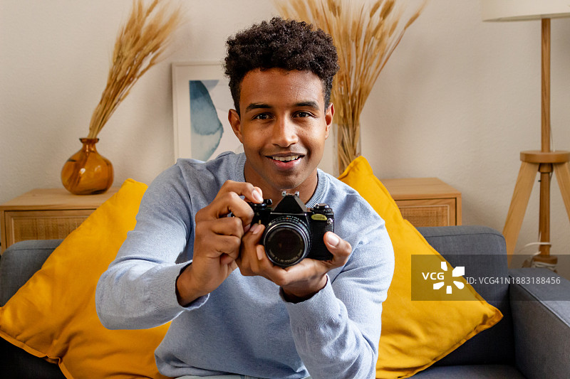 微笑的非裔美国男子在家用相机拍照图片素材
