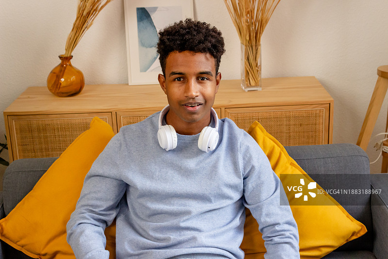 戴着耳机坐在家里的沙发上的年轻男人肖像图片素材